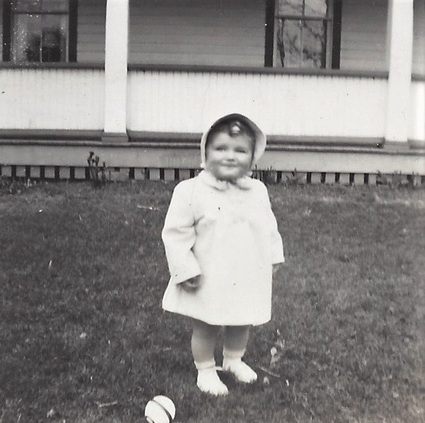 A very young me in front of our family home